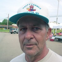 Man with gray hair and five o'clock shadow in a trucker hat